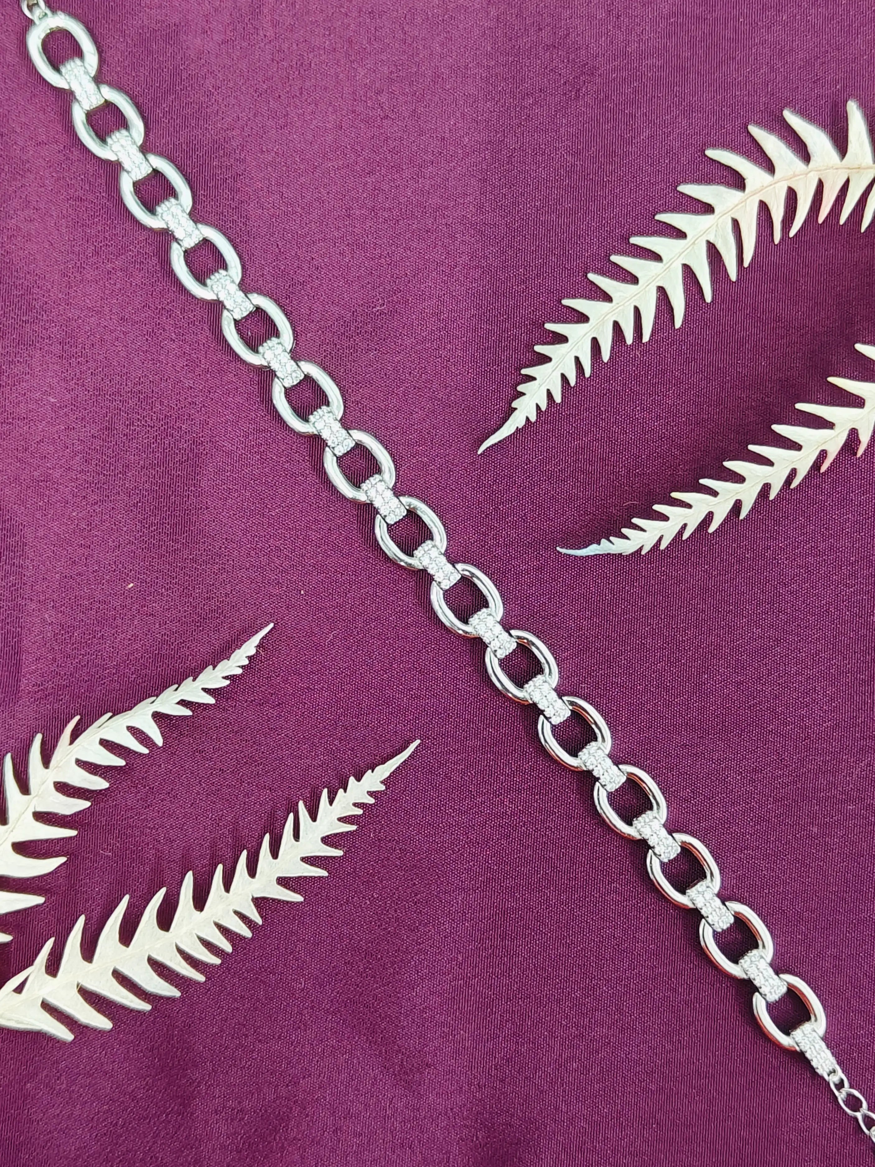 Silver chain necklace on a purple fabric background with leaf patterns